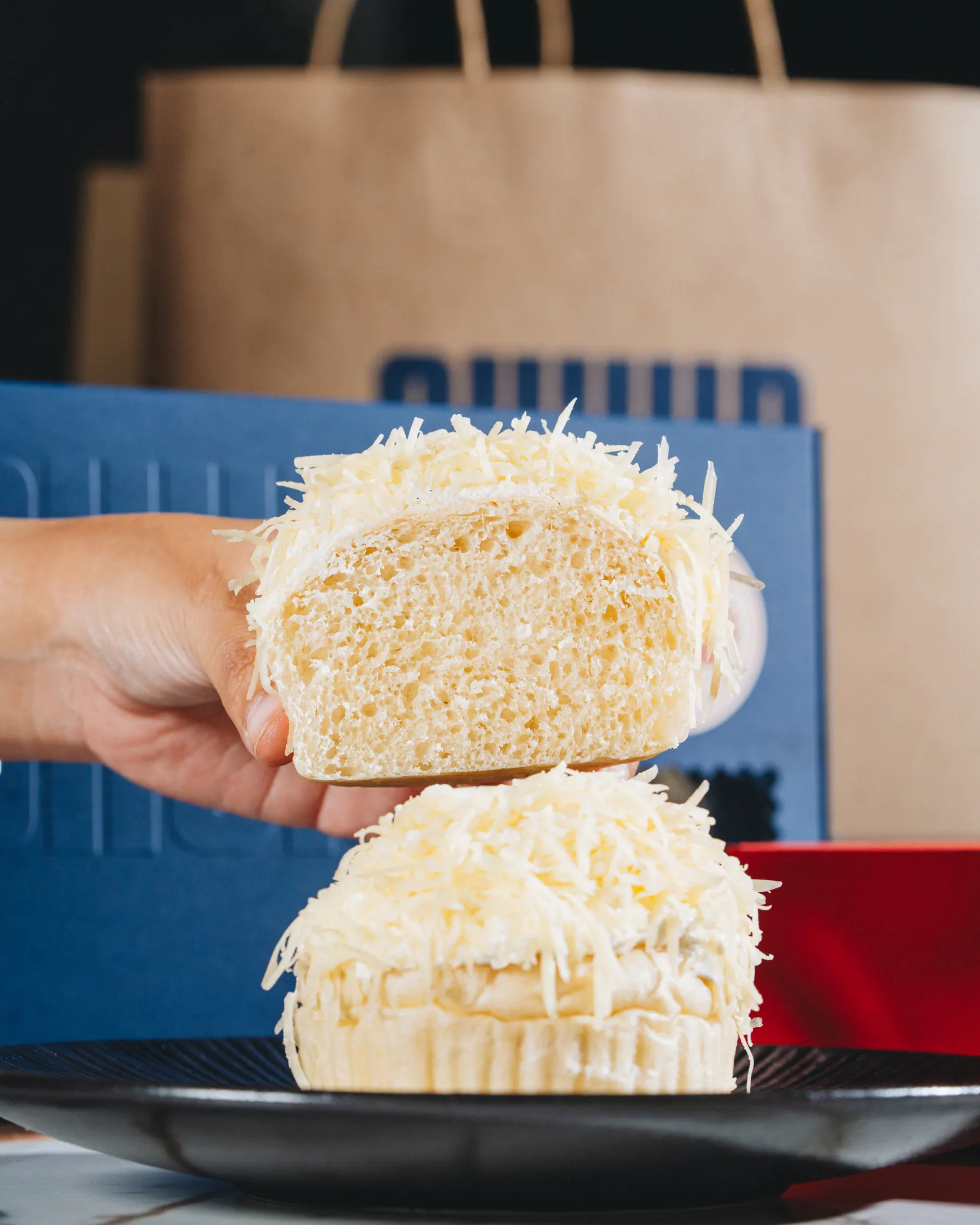 An ensaymada pulled open by hand, the crumb showing under its crown of cheese